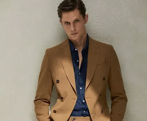 Man wearing a camel double-breasted suit in a linen blend with peak lapels and an open-collar navy shirt