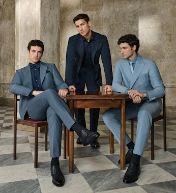 Three men wearing well-kept tailored suits in navy, slate, and light blue around a wooden table