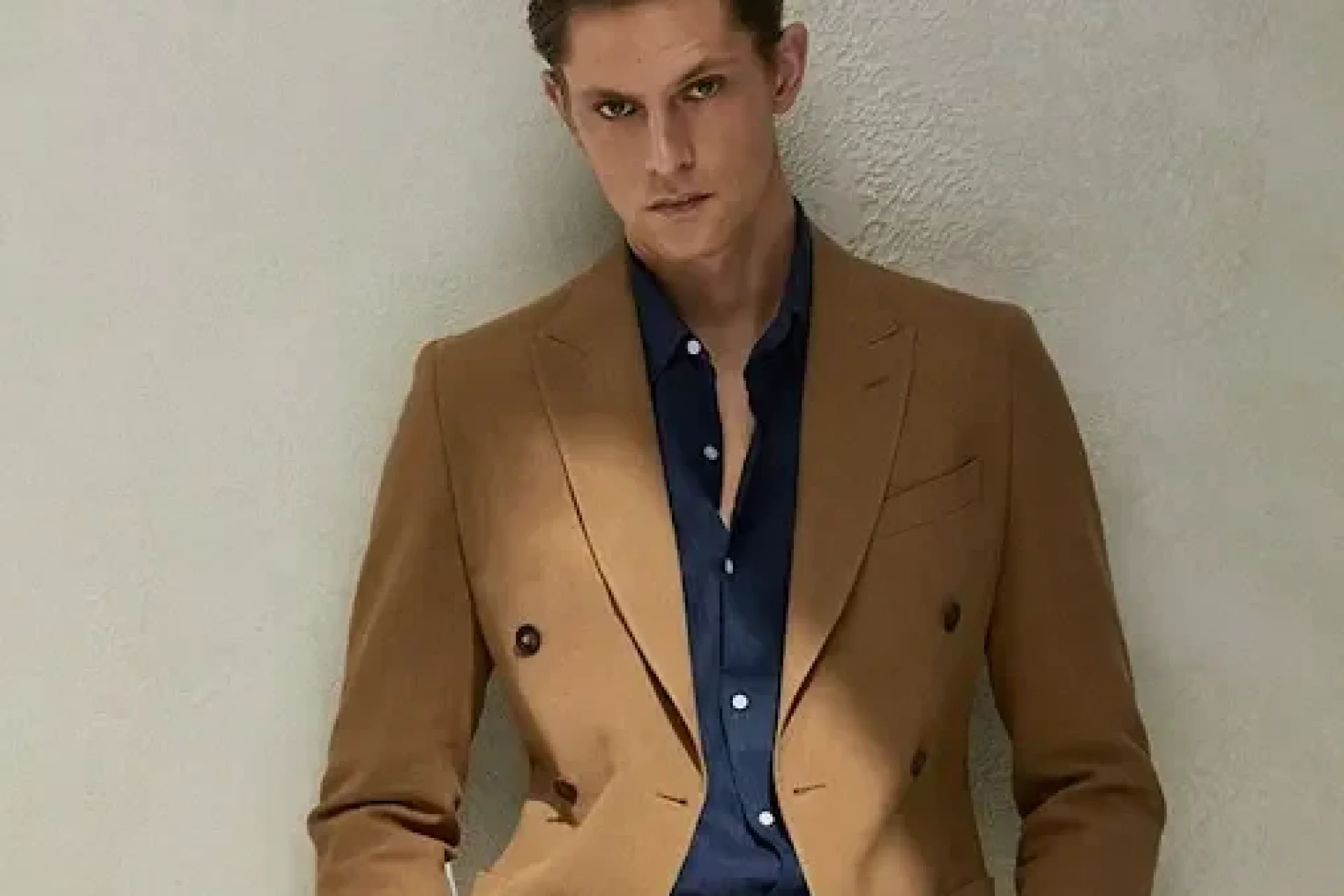 Man wearing a camel double-breasted suit in a linen blend with peak lapels and an open-collar navy shirt